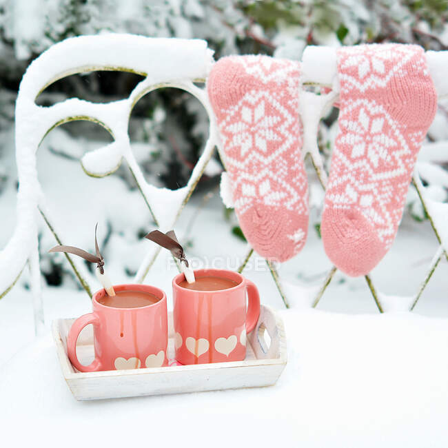 Две чашки горячего шоколада на заснеженной скамейке в саду — стоковое фото