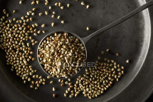 Buckwheat in metal spoon and in metal pewter plate — Stock Photo