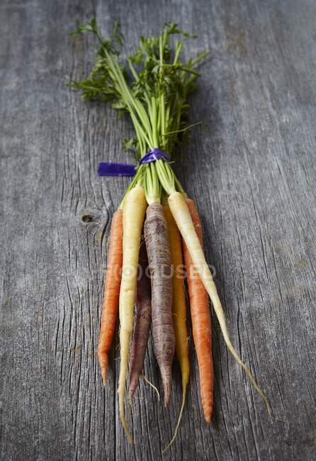Zanahorias rústicas con tallos verdes en la superficie de madera - foto de stock