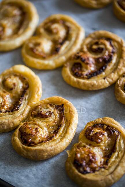 A baking tray with golden cooked comte and pesto palmiers sitting on baking paper. — Stock Photo