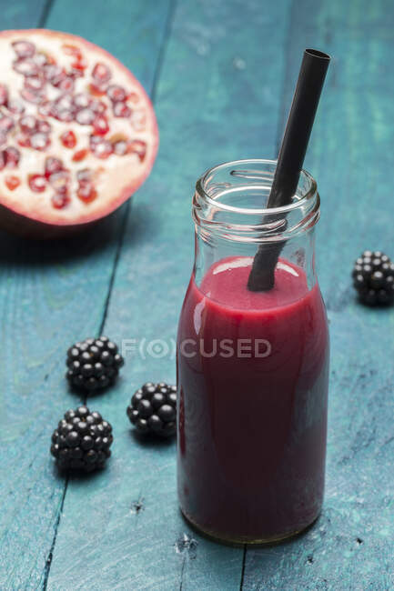 A blackberry and pomegranate smoothie in a bottle with a straw — Stock Photo