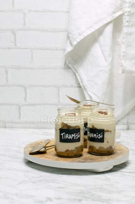 Individual tiramisu desserts in jars with spoons on wooden board — Stock Photo