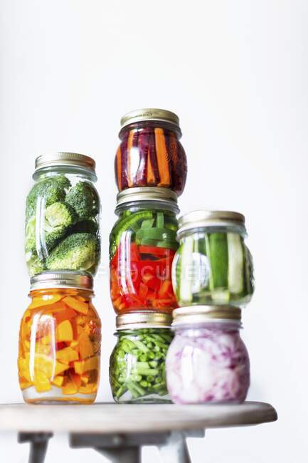 Preserving jars of freshly pickled vegetables stacked on an old stool — Stock Photo