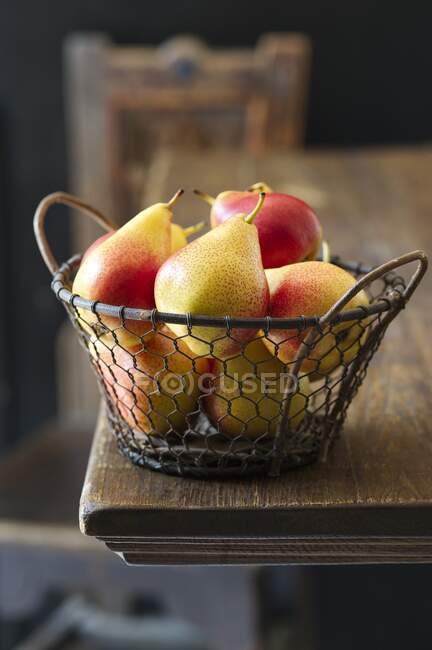 Yellow and red pears in a wire basket on a wooden table — Stock Photo