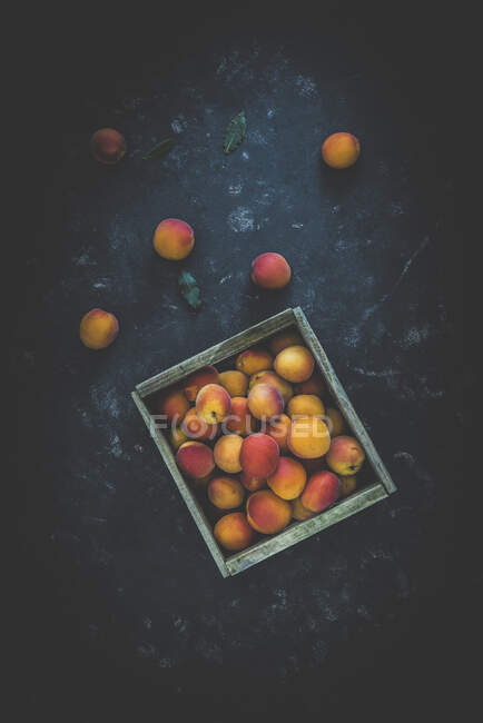 Fresh apricots in wooden crate and on stone surface — Stock Photo