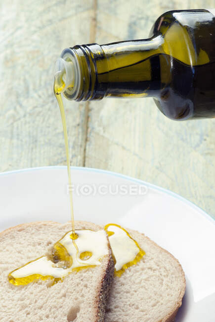Mani versando olio d'oliva sul pane — Foto stock