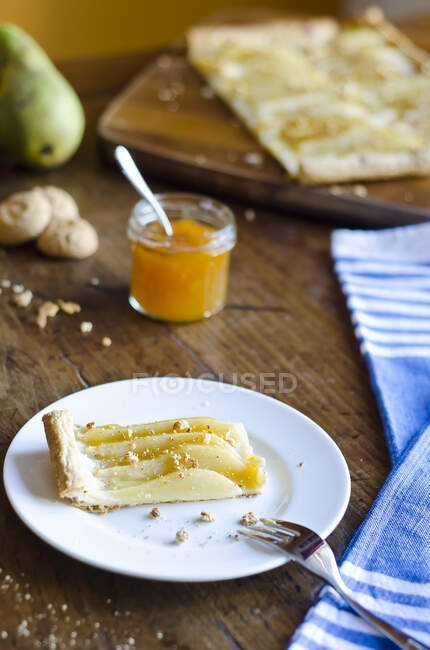 Homemade sweet tart with peach jam, pears and amaretti crumbs on white plate on a wooden rustic background with blue napkin and fork — Stock Photo
