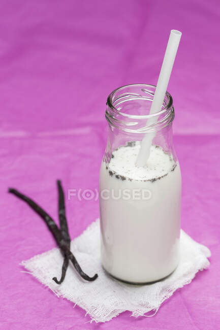 Homemade vanilla milk in a glass bottle against pink background — Stock Photo