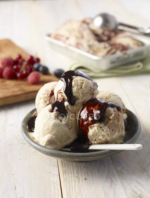Ice cream with chocolate sauce, with fresh berries in the background — Stock Photo