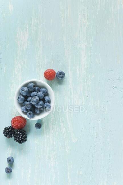 Blueberries in small bowl with raspberries and blackberries on table — Stock Photo