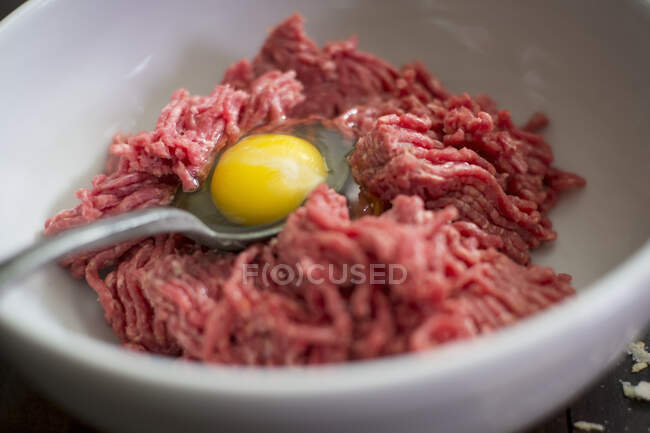 Ingredientes para albóndigas: carne picada y yema de huevo en un bol - foto de stock