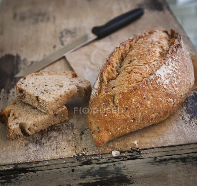 Loaf of rustic bread on wooden surface with knife — Stock Photo