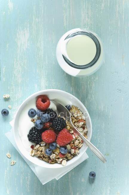 Yogurt e muesli con bacche in una ciotola accanto a una bottiglia di vetro di yogurt — Foto stock