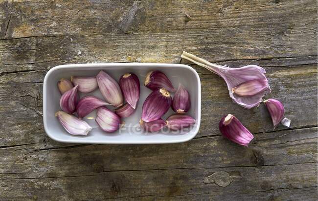 Fresh garlic cloves in a white dish on a wooden surface — Stock Photo
