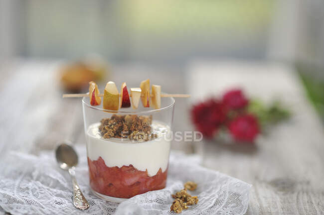Compota de ciruela y pera en un vaso con yogur de coco, granola y un pincho de fruta (vegetariano) - foto de stock