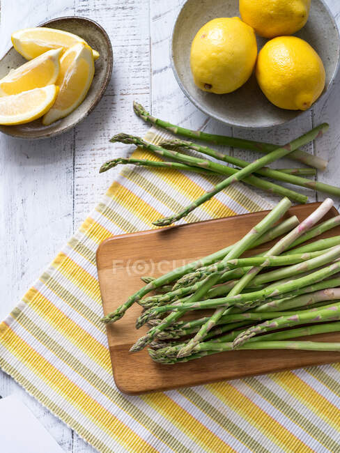 Green asparagus on striped placemat with lemons — Stock Photo