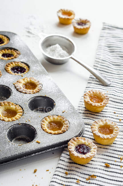 Mini apricots and raspberries jam tartlets in tin and on table with sugar powder in sift — Stock Photo