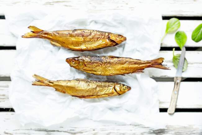 Tres pescados blancos recién ahumados del lago Ammer en Baviera sobre papel con cuchillo y espinacas de hoja de bebé - foto de stock