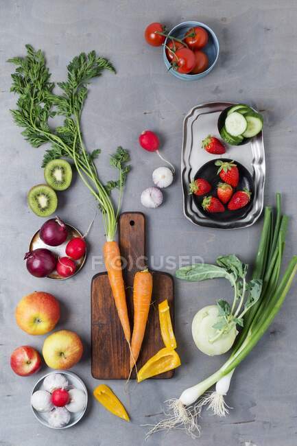 Un arreglo de cebolletas, ajo, manzanas, tomates, pimientos, zanahorias, kiwi, rábanos, fresas y colinabos - foto de stock