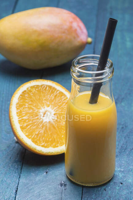 Um batido de manga e laranja em uma garrafa com uma palha — Fotografia de Stock