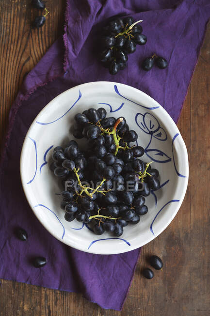Красный виноград в деревенской чаше, раскрашенной вручную на деревянном столе — стоковое фото