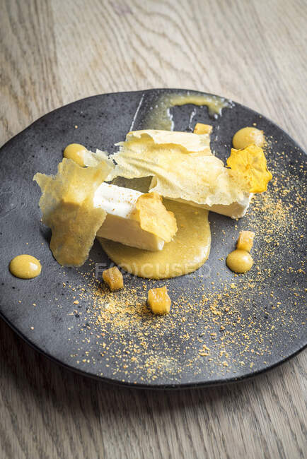 Persimon cheesecake with a persimon puree and crisps on a black plate and light wooden background — Stock Photo
