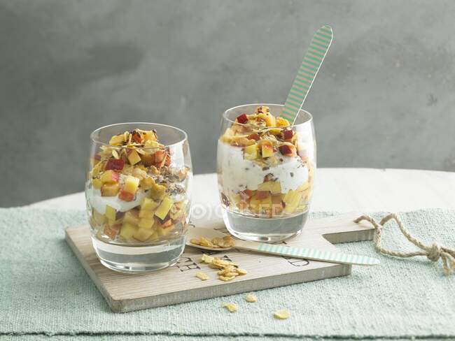 Fruit and yoghurt with cornflakes and seeds in glasses — Stock Photo