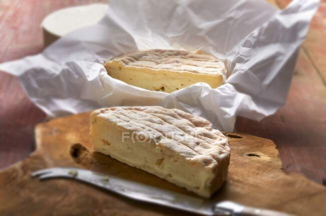 Французький м'який сир на дерев'яній дошці з ножем і в обгортках — стокове фото