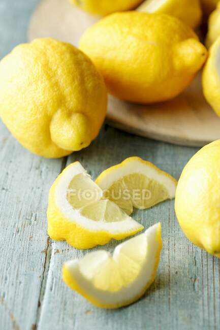 Varios limones enteros y rodajas de limón sobre un fondo turquesa - foto de stock