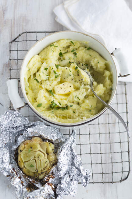 Homemade mashed potatoes with butter in a pot and baked garlic in aluminium foil — Stock Photo