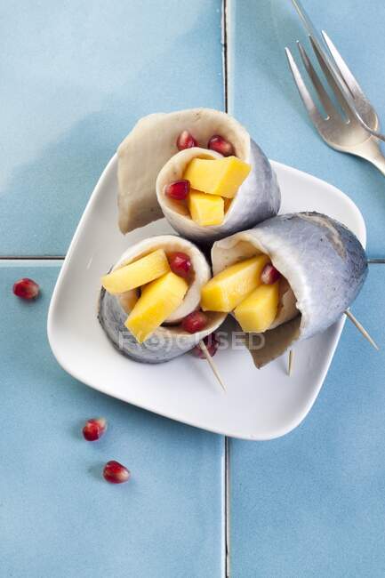 Rollmops (pickled herring fillets) with mango and pomegranate seeds — Stock Photo