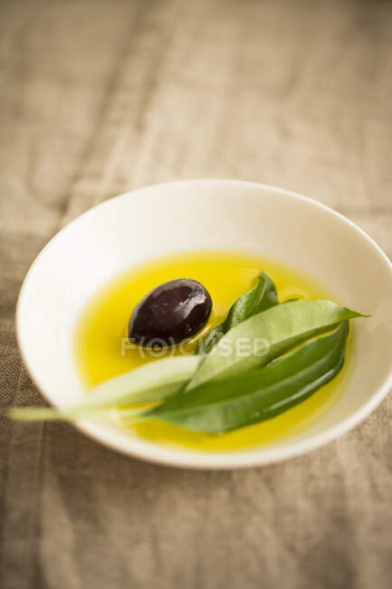 Olive oil with a black olive and an olive sprig in a bowl — Stock Photo