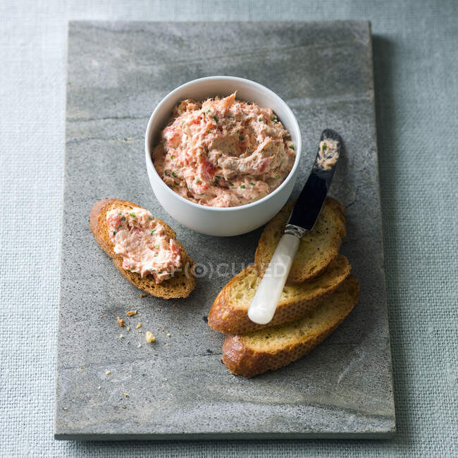 Salmon rillette on toasted baguette slices with knife and in bowl — Stock Photo