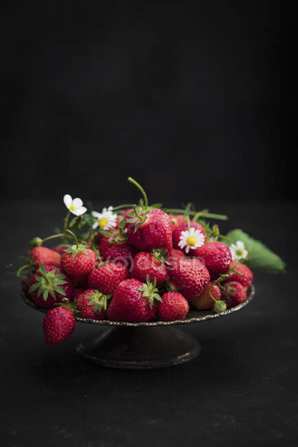 Strawberries with blossoms and green leaves in bowl — Stock Photo