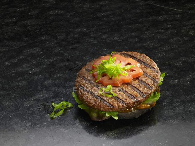 A grilled hamburger on a black bread roll — Stock Photo