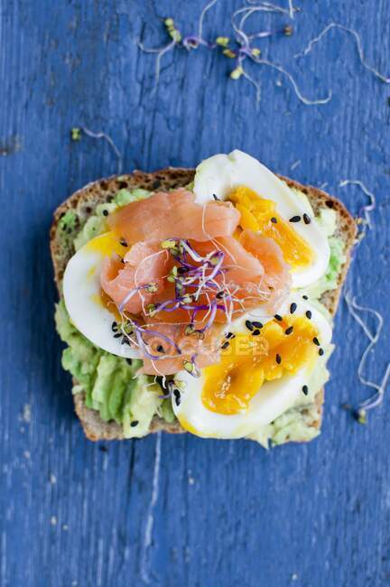 Open sandwich with avocado, egg, salmon, sprouts and sesame seeds — Stock Photo