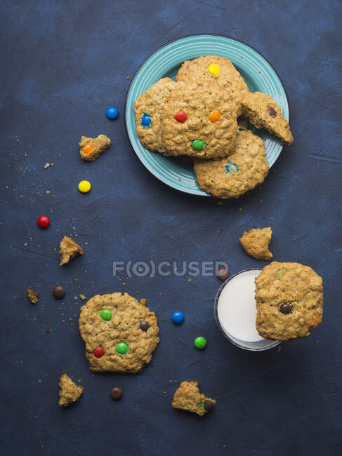 Oatmeal butter cookies with colorful candies with a glass of milk on blue background — Stock Photo