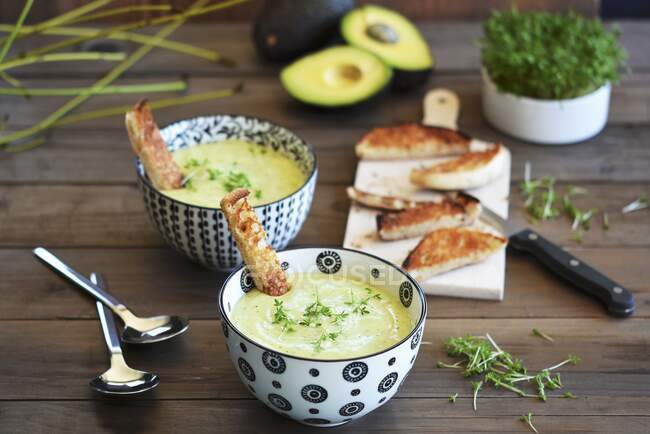 Zuppa di avocado in due ciotole su un tavolo rustico con pane tostato e crescione fresco — Foto stock