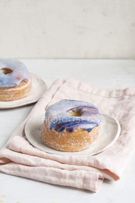 Two galaxy croissant doughnuts with marble glaze on plates — Stock Photo