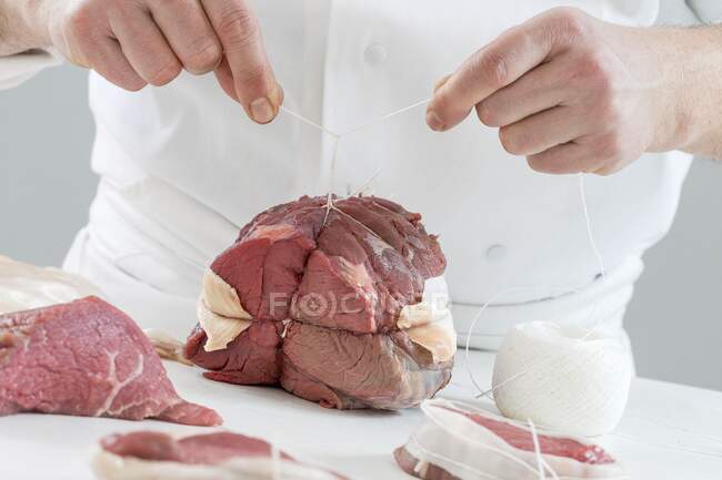 A joint of roast beef being tied with string — Stock Photo
