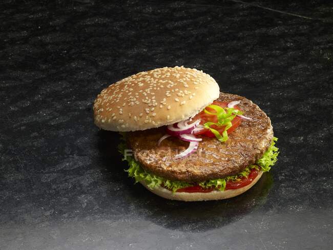Un hamburger dans un pain de graines de sésame avec oignons, tomate, laitue et ketchup — Photo de stock