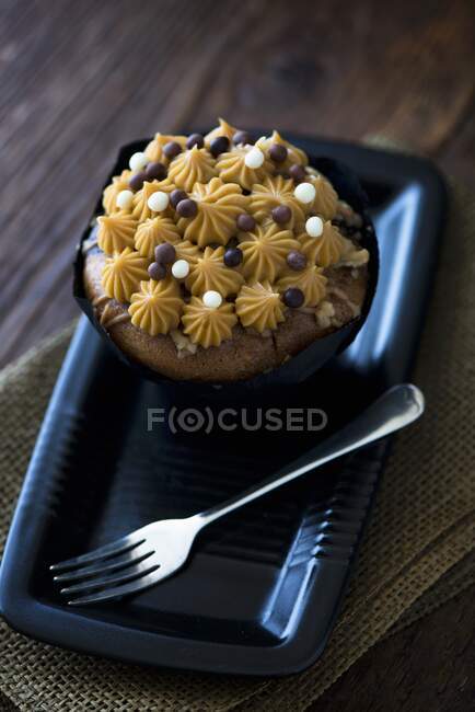 A salted caramel cupcake on a black plate with a fork — Stock Photo