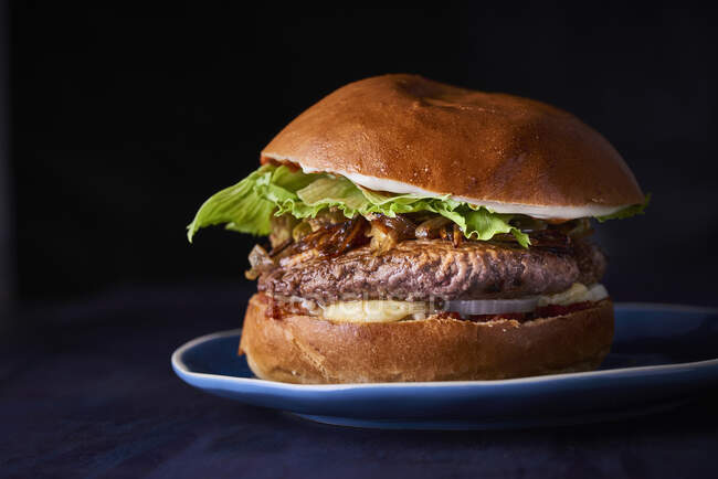 Un beefburger sur une assiette sur un fond sombre (gros plan) — Photo de stock