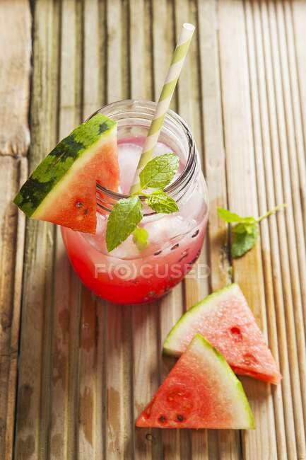 Succo di anguria in un barattolo di vetro con cubetti di ghiaccio, menta e una fetta di anguria fresca — Foto stock