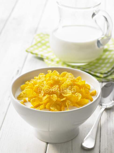 Flocos de milho com leite na tigela e colher na mesa — Fotografia de Stock