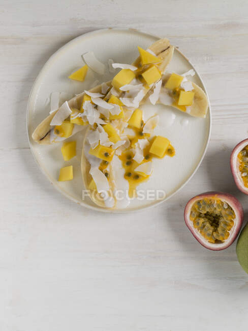 Bananes coupées en deux avec mangue, fruit de la passion et noix de coco — Photo de stock