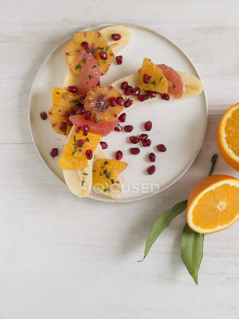Halved bananas with oranges, grapefruit and pomegranate seeds — Stock Photo