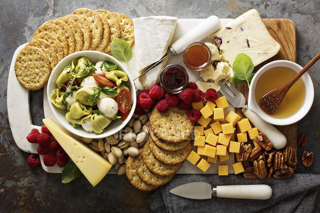 A cheese plate with tortellini salad, crackers, fruit and nuts — Stock Photo