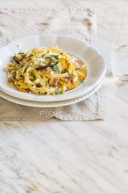 Fresh homamade tagliatelle with yellow and green courgettes, bacon and goat cheese — Stock Photo