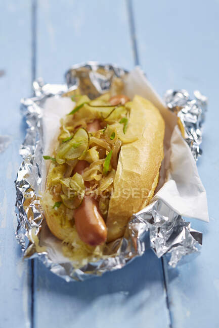 Hot dog with cucumber and onions in aluminium foil — Stock Photo